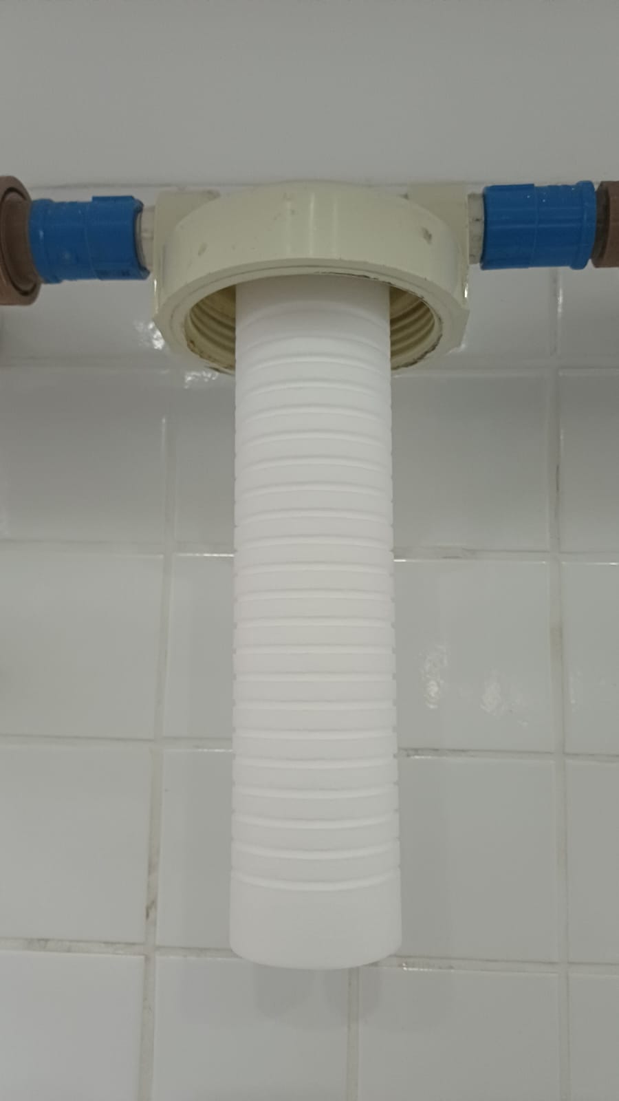tubulação de instalação hidráulica com sifão flexível branco conectado a conexões azuis em parede de azulejos 