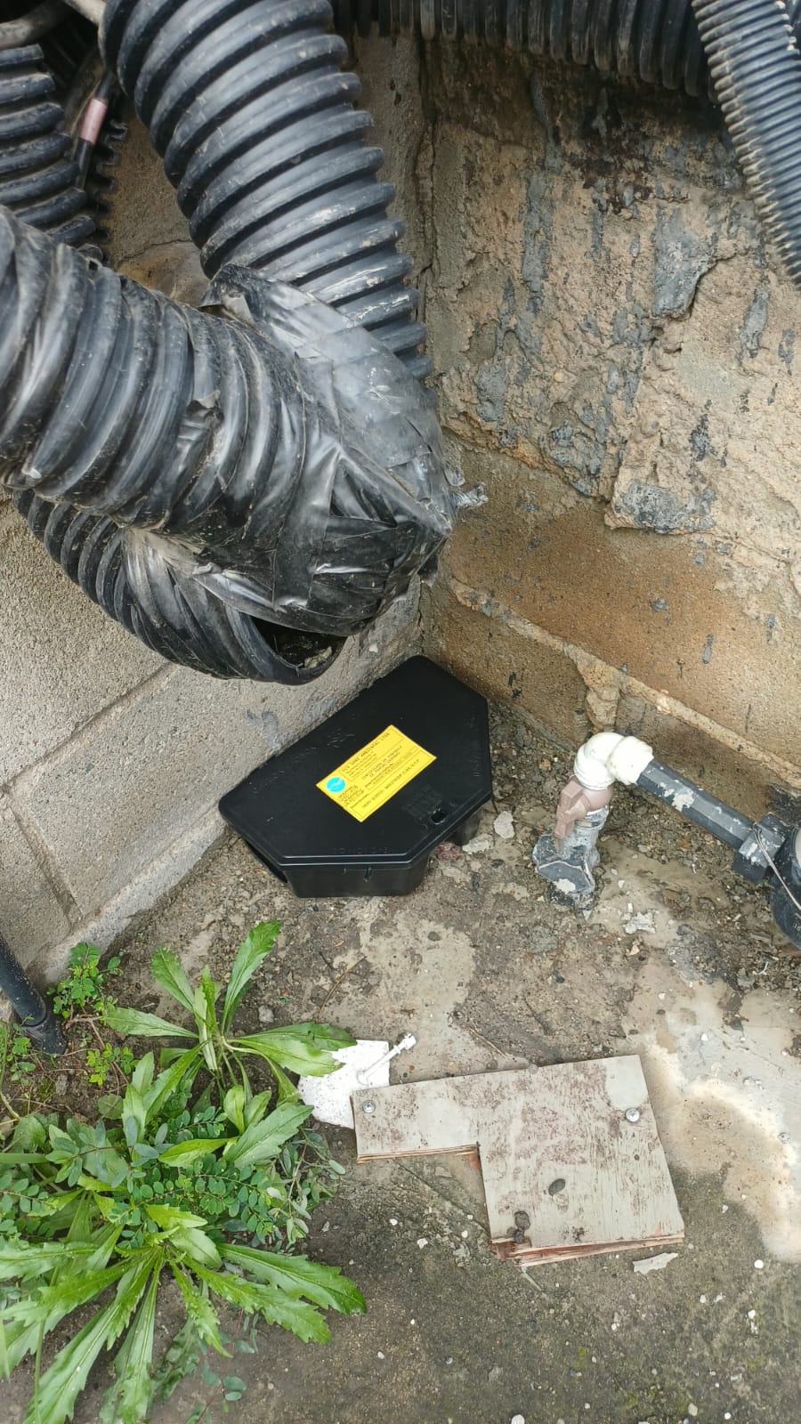 caixa preta de drenagem de ar-condicionado no canto de uma parede externa com corrugados pretos, tubulação e p