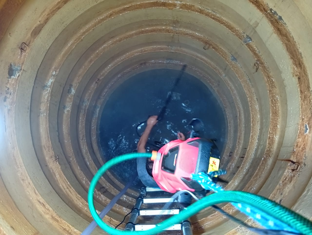 vista de cima de um homem com motor-bomba vermelho limpando o interior de um poço ou caixa d'água cilíndrica 